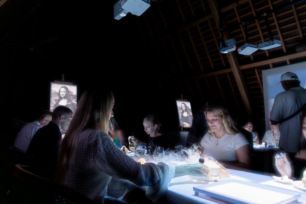 Guests dining in a dark room with glowing tables and creative dishes during a luxury dining experience.