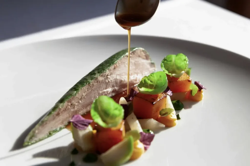 A chef pours sauce over a carefully plated gourmet dish with fish and fresh vegetables in Bali.