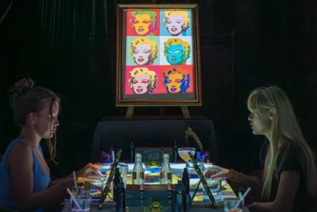 Two guests paint together at a private Ubud event, with drinks, art supplies, and colorful artwork surrounding them.