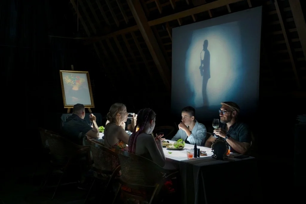 Guests enjoy dinner while watching a projected shadow performance during an evening show in Bali.