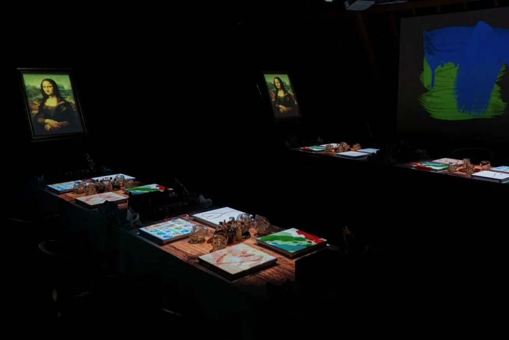 Dark dining tables display paintings and art materials, with projected artwork creating an immersive dinner experience in Ubud.