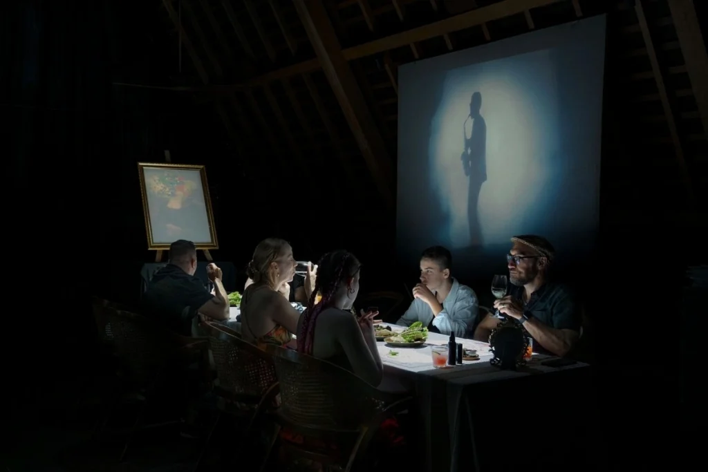 Diners share a meal in a dark Ubud restaurant with projected artwork creating an intimate dining setting.